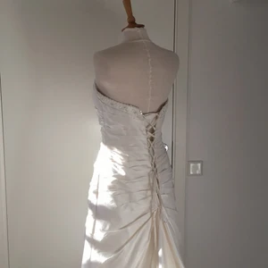 Vit sidenklänning - En klassisk brudklänning i siden. Klänningen har snörliv och inbyggd korsett. Under stussen så släpper klänningen ut ett släp. Storlek 38, går att få den sitta snyggt med snörningen i ryggen. Finns axelband som medföljer klänningen. Som fästes med hyskor. Klänningen är aldrig använd!