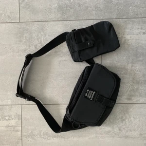 Axelremsväska  - Tech fashion axelremsväska från London, UO. 