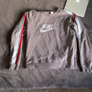 Nike tjocktröja - Grå tjocktröja från Nike med stripes på ärmarna. Riktning skön tröja med bra passform. Passar till nästintill allt och priset bestämd av köpare