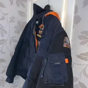 Bomberjacka från parajumper Går att vika in den orangea luvan med hjälp av dragkedja runt halsen.  Köpt från Care of Carl för 6500kr Storlek: M  För att kolla authenticity/Äkta: Certilogo.com och skriv sedan in siffrorna 335567282944. DM vid intresse