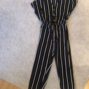 Byxdress Lindex  - Somrig randig byxdress från Lindex. Med stora knappar och knyt i midjan. Croppade ben. Storlek M. Fint skick! 99 kr + frakt 