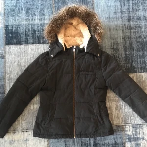 Jacka med fluffig luva - Vinterjacka från MQ (365) med fluffig luva. ”Insydd” i midjan för en mer markerad midja. Luvan går enkelt att ta av. Har haft den i flera år men använder den inte så mycket längre även om den är i gott skick. Inköpspris 1000kr.