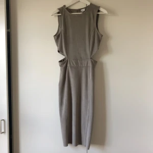  - Grå vadlång klänning i mockaimitation med cut-out detaljer . Använd 1 gång , så gott som ny! Ev frakt betalas av köpare.