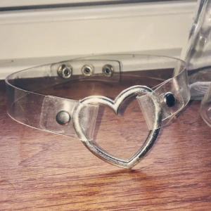  - Choker! Metallhjärta med genomskinligt plastband.  Spännet längst in har fallit bort (se bild) men gör bara nåt om du har väldigt smal hals