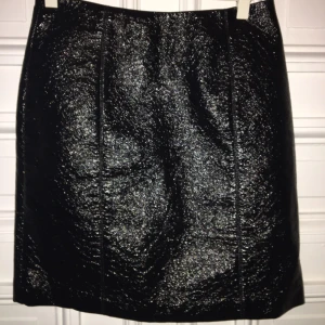  - Svart kort kjol i lack tyg med dragkedja bak.