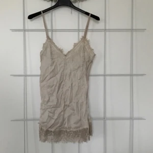  - Beige linne i satinliknande material med spetskant och justerbara axelband. Hade mått bra av en omgång med strykjärnet då den legat helt oanvänd i garderoben haha..!