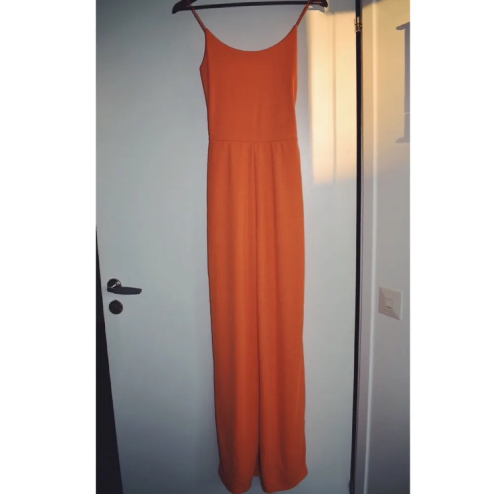 En splitterny orange jumpsuit som kan användas till vardags och även på festliga tillfällen. . Övrigt.