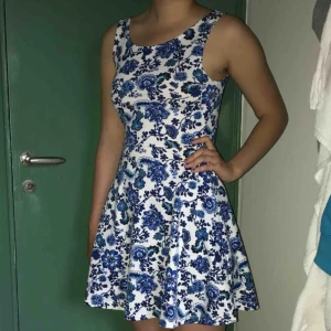  - Detta är en blommig klänning som slutar ovanför knäna. Den är storlek S och sitter rätt tajt över bröst och mage. 