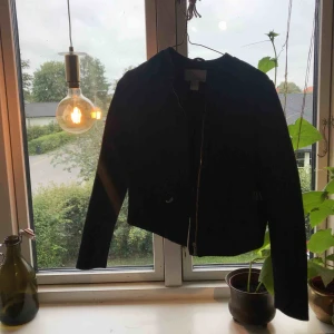  - En svart jacka med ett diskret mönster i svart. Två fickor fram och en dragkedja som är svängning.