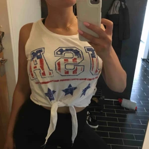 - Linne med knytning i fram och USA-tryck! Storlekslappen är tyvärr borta, men skulle säga att det är storlek M ☺️