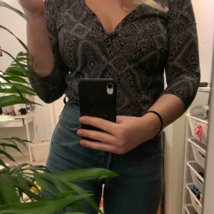  - En mönstrad blus med knappar vid urringningen så man kan reglera den själv. 