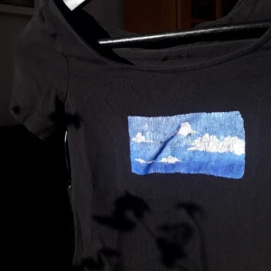  - T-shirt med en målad bild på av en himmel med måln.