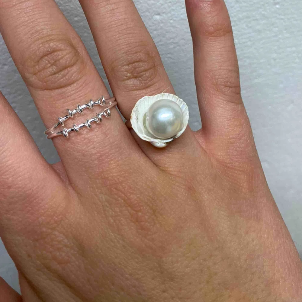 Handjord silvrig ring med äkta snäcka med en vit pärla i. Justerbar i storleken . Accessoarer.