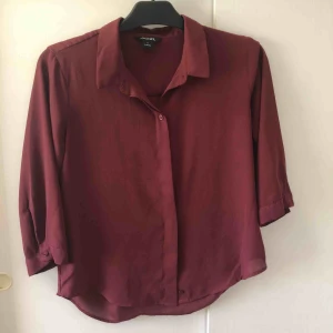  - En röd blus från ’. Knappar hela vägen ner så det går att ha den knäppt och inte knäppt. Ärmarna går ungefär till armvecken.  Frakt ingår inte. Köparen står för frakten.