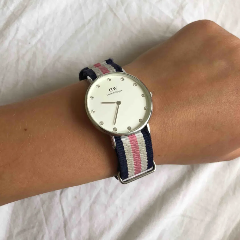 Jättefin klocka ifrån Daniel Wellington med silvriga stenar i uret och blått/rosa band! Sparsamt använd och du får med båda boxarna som är väldigt fina de också😊😊batteriet behöver dock bytas skulle jag tro. Accessoarer.