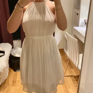 Vit klänning - Fin luftig vit klänning från Nelly med öppen rygg med strass runt halsen och ryggen. Dragkedja på sidan och möjlighet till två knappjusteringar i nacken. Köparen står för eventuell frakt 