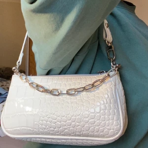 Axelväska - Säljer denna axelväska från Shein! har använts mest under sommaren men är fortfarande i bra skick! den har en fin kedja på ena sidan som gör väskan lite mer speciell och lägger en fin detalj på outfiten! vid intresse kan jag skicka mer bilder:)