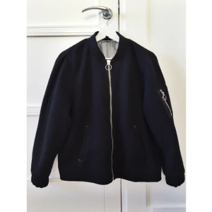  - Jättefin jacka i bombermodell och 8% ull. Fina och enkla detaljer. Jackan är inköpt i höstas och knappt använd. Ljusblått fint innertyg. Resårkant i ärmslut och nederkant band.   Hämtas på Gärdet eller fraktas. 