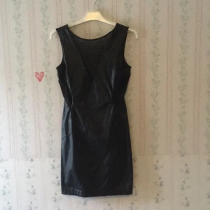 - Svart tight klänning i fakeskinn från Selfridges i storlek S. Detalj med genomskinligt svart tyg på framsida och djup v-urringning på ryggen. Använd ett fåtal gånger. Frakt tillkommer.