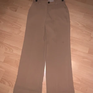 Biege kostymbyxor från NAKD strl 38 - Biege kostymbyxor från Nakd, hellånga. Knappt annvända, säljer då de ej kommer till användning. Strl 38