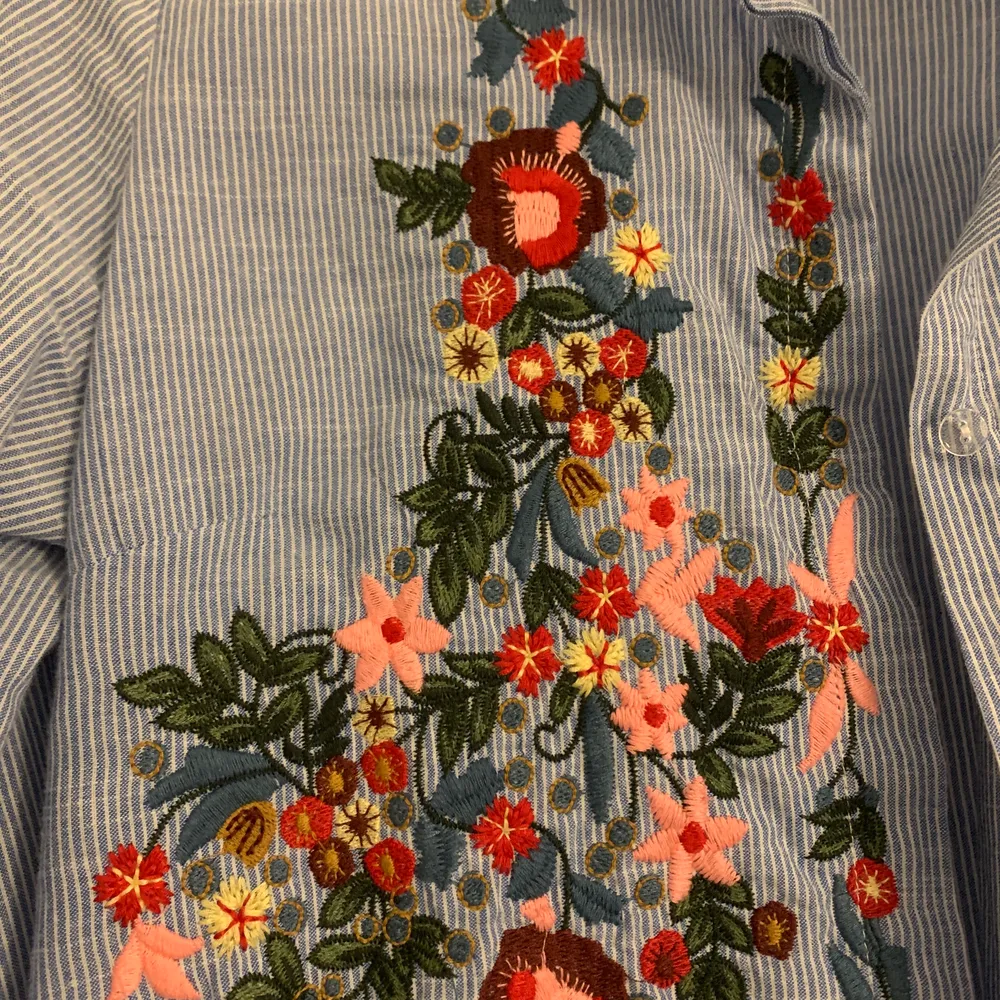 Vit och blårandig skjorta med broderade blommor. Jag har köpt den från en butik i Italien. M Storlek och kort i höjd. . Skjortor.