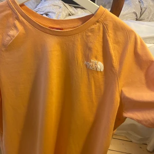 The North Face Tshirt - snygg orange tshirt med tryck på ryggen! Köpt på asos och är strl M i herrstorlek. har en liten fläck på framsidan som syns på första bilden, själva loggan är också lite skadad tyvärr. Köparen står för frakt 🧡