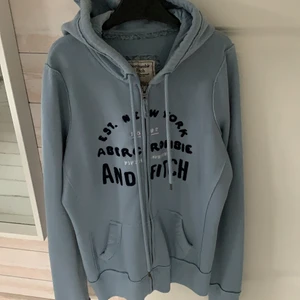 Abercrombie & Fitch kofta strl S - Figursydd ljusblå kofta med mörkblå text från abercrombie & fitch. Fullt fungerande dragkedja. Strl S, passar folk på 165-175. Använt ett par gånger men är ändå i bra skick. Hör gärna av dig vid intresse, pris kan diskuteras!
