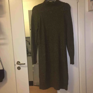  - ”Stickad”klänning i mörkare grön färg med hög hals. Ungefär 150cm lång. 58% akryl, 22% bomull, 12% polyamid, 7% polyester och 1% elastan. Kan mötas upp alt. skicka.