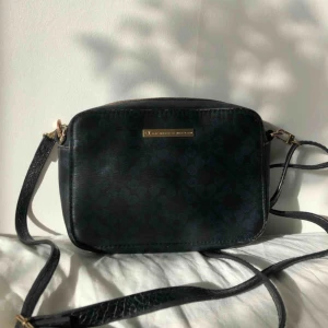 et DAY Birger et Mikkelsen väska - Axelbandsväska från et DAY Birger et Mikkelsen i läder. Svartblå färg med detaljer i guld. Få spår av användning på exteriören, se bild för referens. Perfekta lilla svarta handväskan! Nypris ca 649kr.