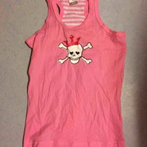 Döskallelinne - Sött rosa linne med döskalle fram. På baksidan är det rosa/vit randigt. Märkt som 146/152 men jag kunde ha det när jag var xs/s. Fint skick. Frakt: 42 kr.