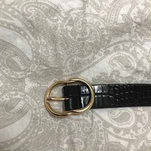 Bälta i ormskinns-imitation  - Svart bälte med guldspänne. Använts flera gång därefter är bältet böjt när de inte är i byxorna, inget som syns när de väl sitter på. Gjort egna hål med en stans, så ”snygga” hål och inget problem på det estetiska planet. Rensar garderoben så vill bara ha bort allt! Frakt tillkommer! MÖTER UPP INTE! 