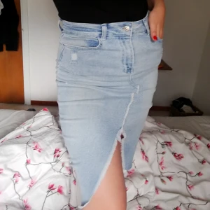  - En ljusblå denim kjol i knälängd med en slit i mitten, den är hög i midjan och den är även lite stretchig. Helt oanvänd med lapp kvar. 