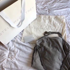 Stella McCartney väska - Säljer min Stella McCartney väska i modellen ”Falabella fold Over tote” i färgen grå. Har små defekter (se bild) knappt synliga.  Köptes för 7150kr. På marknaden just nu ligger priset på ca 9000-10 000kr. Jag säljer för 3000kr