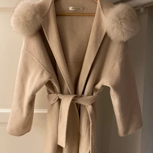 Born in Stockholm kappa - Beige kappa med fluffig pälsluva. Sparsamt använd. Storlek s men passar allt från xs-m . 50/50 ull och cashmere. Inköpt för 4500kr. 