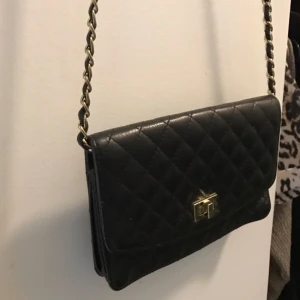  - Liten qulitad väska svart med gulddetaljer  Mindre kortfack innuti (se bild) brunt innerfoder köpt i London, äkta läder  Fint skick o knappt använd, lite sliten på axelkedjan, guldfärgen, i övrigt mycket fin! Inga märken el dylikt nypris 600:-