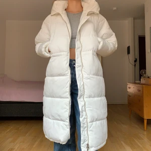 Vit pufferjacka - Vit lång pufferjacka från Bik Bok med dragsko i midjan. Knappt använd så i nästintill nyskick! Nypris 1299kr. +95kr frakt