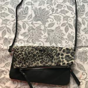 Väska med tunnt band, svart och grå leopardmönstrad. 