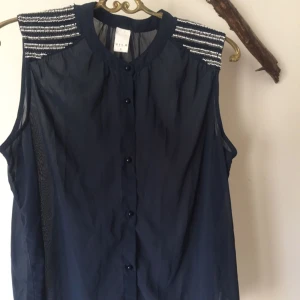  - Mörkblå blus med pärldetaljer på axlarna. Endast prövad.   Garderobsrensning, se mina övriga annonser. Möjlighet till samfrakt.   Köparen står för frakt. Ansvarar ej för postens ev slarv.