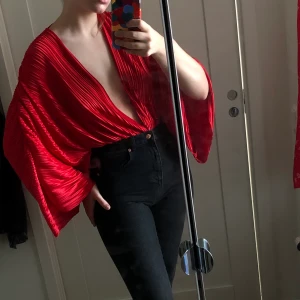 Röd långärmad body - En fin röd body som går att både klä upp och klä ner. Djupt urringad med pösiga armar, man knäpper bodyn mellan benen med hjälp av två knappar. Knappt använd och i jätte fint skick, dock inga lappar kvar. Frakt ingår ej, kan mötas upp i karlstad :)