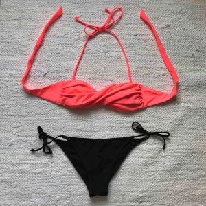  - Bikini från H&M, storlek 34. Neonrosa överdel i twistad bandeau-modell med avtagbara axelband. Svart tanga-underdel som knyts i sidorna. Använda men i mycket fint skick! Mottagare står för fraktkostnad
