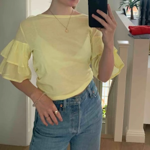  - Ljusgul tunn tröja/blus från hm med volanger på ärmarna. Aldrig använd, jätteskön. Frakt tillkommer.