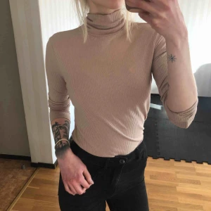  - Beige/rosanude ribbad polotröja. Stretchig och mycket bekväm. 
