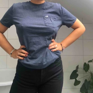 T-SHIRT - En mörkblå t-shirt som är rätt hög i kragen, vilket är så snyggt! Har en liten ficka på vänstra bröstet. 