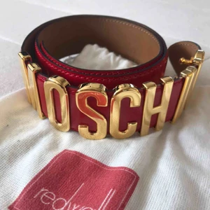  - Rött Moschino-bälte. Mkt bra skick, ngn liten repa i lädret, i original Redwall-påse.  Total längd: 83,5 cm Omkrets yttersta hålet: 75 cm Omkrets innersta hålet: 69 cm