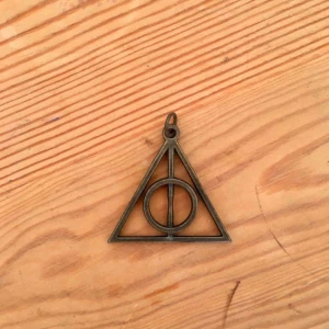  - Berlock till halsband i form av dödsrelikernas symbol från Harry Potter. I bra skick, ca 5 cm högt.