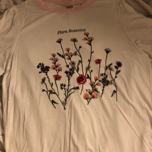Blommig t-shirt - Vit t-shirt med ett blommigt tryck och rosa kanter i strl XS. Ganska stretchigt material. Skriv om du vill ha bättre bilder på plagget, tex passform på kroppen osv!
