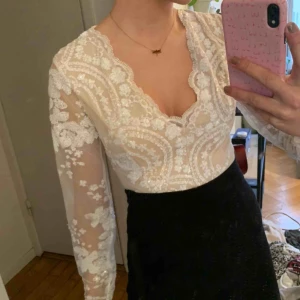  - Beige body med broderi i vita paljetter. Ärmarna är genomskinliga och det finns en dragkedja i ryggen. Priset är exklusive frakt. 