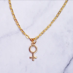 Halsband kvinnosymbol guld - Guldfärgad halsband med kvinnosymbolen, kedjan är ca 50cm. Observera att guldfärgen inte är så konstig som det ser ut på bilden, försöker lösa det! Fri frakt vid köp över 100:-