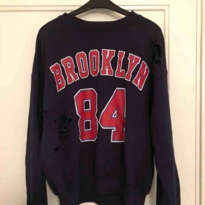  - Mörkblå sweatshirt med röd text och tillgjorda hål på från Gina tricot