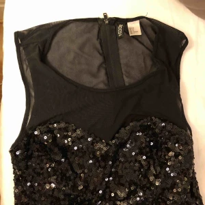  - Svart byxdress (kortbent) med paljetter över bröstet.  Även fickor! Nyskick! 